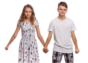 Portrait of angry teen boy and girl holding hands together. Embittered teenagers looks at camera. Serious children in casual clothes, isolated on white background. Friendship and love concept.