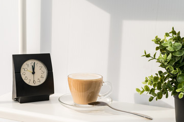 A Cup of coffee with a clock on the white table. It's time for a coffee break.