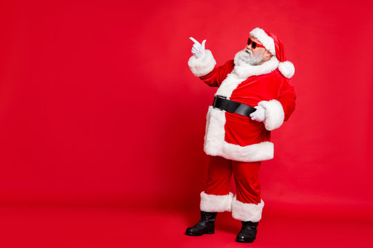 Full length profile side photo of charming santa claus in eyewear eyeglasses showing promo wearing bright costume belt isolated over red background