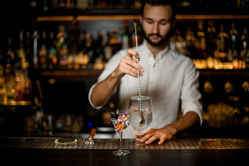 Bartender stirs an alcohol cocktail with bar spoon