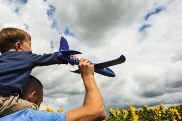 Father and son playing with a toy airplane near the sunflower field