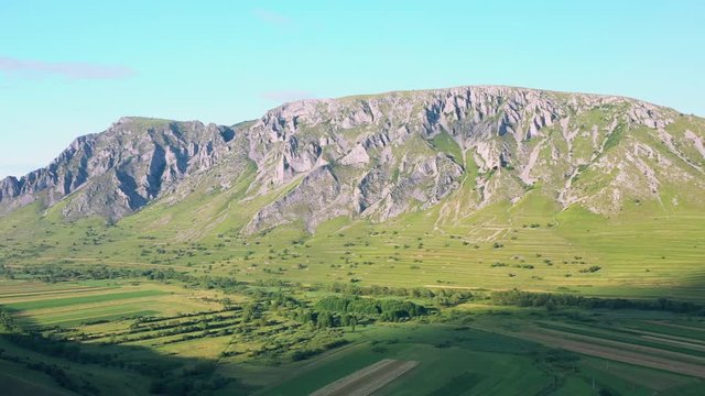 A wide angled fly over drone shot of the Coltesti mountain range, Romania. The valleys and gorges expand far into the distance, green fields fill the foreground.