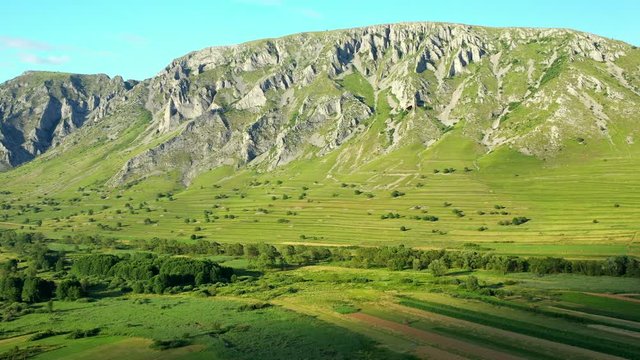 A wide angled drone shot flying down onto the Coltesti mountain range, Romania. The valleys and gorges expand far into the distance, green fields fill the foreground.