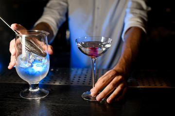Bartender holding cocktail and strainer on the bar counter