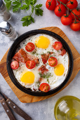 Fried eggs, bacon and vegetables on a frying pan. Breakfast time. Top view.