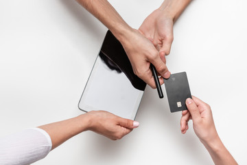 Close up top view of a woman hands over bank card to a man in order to pay for the product. Tablet and pen on a white table. Concept of e-commerce and online shopping. Successful deal.