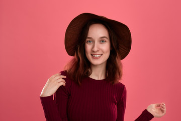 Portrait of a happy beautiful brunette girl in a wide-brimmed hat posing on a dark pink background.