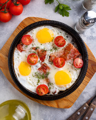 Tasty breakfast with fried eggs, bacon and vegetables on a frying pan. Top view. Closeup