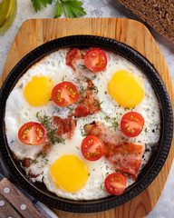 Fried eggs, bacon and vegetables on a frying pan. Breakfast time. Closeup. Top view.