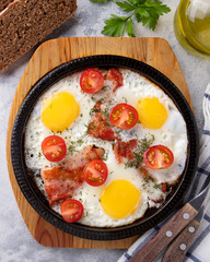 Fried eggs, bacon and tomatoes on a frying pan. Tasty breakfast on a frying pan. Top view