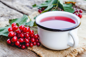 White mug or cup of hot viburnum tea on a wooden table next to red viburnum berries. Source of natural vitamins. Used in folk medicine.