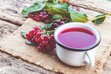 White mug or cup of hot viburnum tea on a wooden table next to red viburnum berries. Source of natural vitamins. Used in folk medicine.