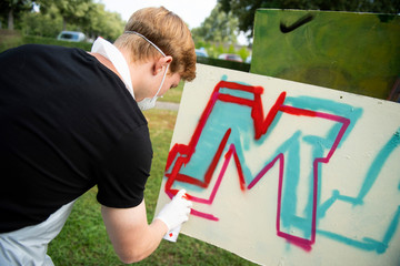 junger Sprayer beim gestalten eines Plakat-Graffiti mit Spraydose und Mundschutz