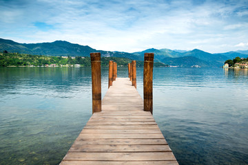 Wooden pier on Orta San Giulio Lake with mountain scenery background. Italy.