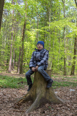 Fototapeta premium boy in the forest on a stump,boy in glasses sits on old stump in forest