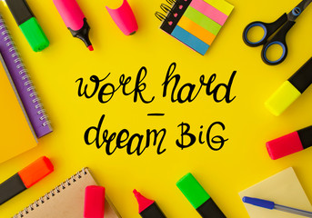 Work hard dream big. Different stationery on the yellow background with handwritten lettering, top view. Business and education theme. Work place, flat lay. Marketing, management, development