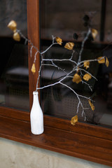 Fototapeta na wymiar A branch with leaves in a white bottle stands on windowsill.