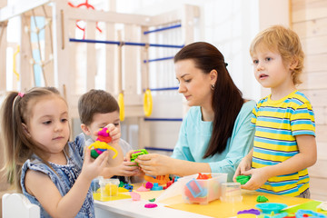 Obraz na płótnie Canvas Kids with play clay toys in kindergarten. Children with teacher in da care centre