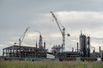 View of a complex of industrial buildings with smoking chimneys and construction cranes.