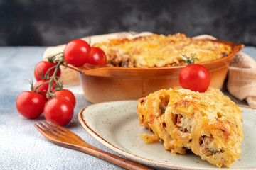 Golden cannelloni with meat, tomatoes, cheese sauce and pasta in alternating layers on a rustic plate