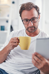 Man holding tablet, surfing online and drinking coffee.