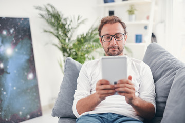 Man using tablet and sufring on the internet in his living room.