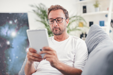 Man using tablet and sufring on the internet in his living room.