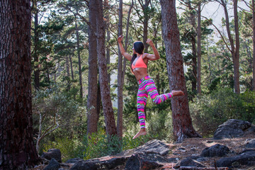 Naklejka na ściany i meble Beautiful athletic woman surrounded by trees in a forest levitating in mid air at sunrise.