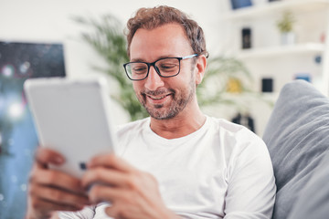 Man using tablet and sufring on the internet in his living room.