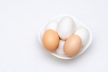 Close up shot of whole white and brown eggs in a white bowl