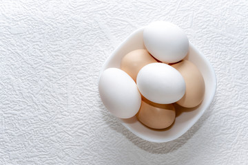 Whole white and brown eggs in a white bowl on a white surface