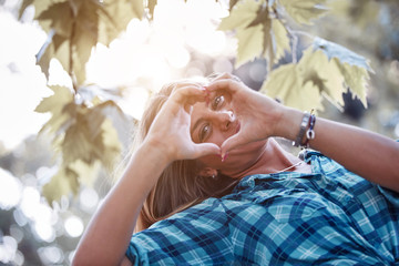 Young woman outdoors making heart - shape symbol for love and romance.