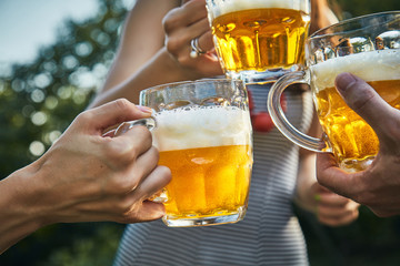 Group of young people enjoying and cheering beer outdoors.