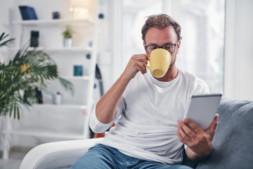 Man holding tablet, surfing online and drinking coffee.