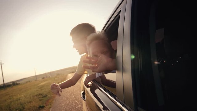 Happy family traveling by car. Two boys in the car window waving their hands in the sun at sunset.
