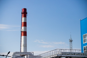 Red and white chemical plant pipe throws harmful poisonous smoke into clear blue sky with copy space. Concept of greenhouse effect and air pollution due to fuel combustion and chemical production.