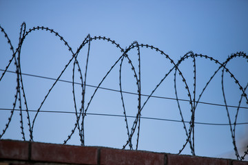 Barbed wire fence around prison walls blue sky in background