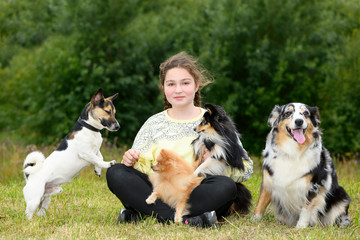 The dark-haired girl, 12 years old, and her dogs are sitting in a park.