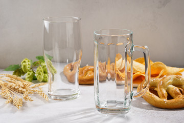 Clean and empty beer glass and a mug with various snacks around.