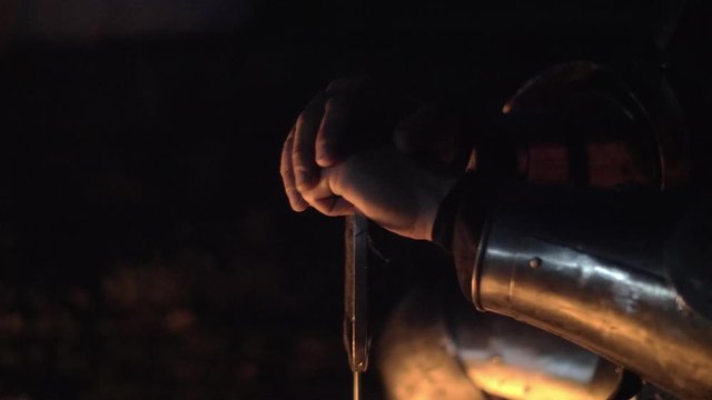 Close-up of knight hands whit sword near the bonfire. Sword in the hands.