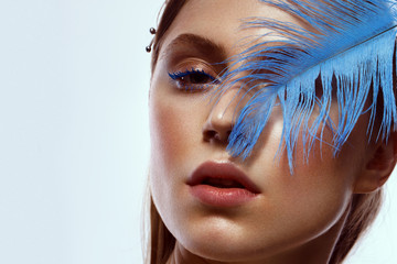 Beautiful tanned girl with creative make-up and blue eyelashes, feather in hand. Beauty face.