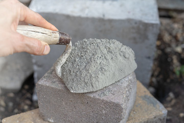 Worker hand hold a trowel with cement powder on brick on concrete background. Brickwork construction concept.