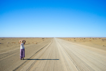 A lone traveler looking down an long, empty desert road. - 289265408