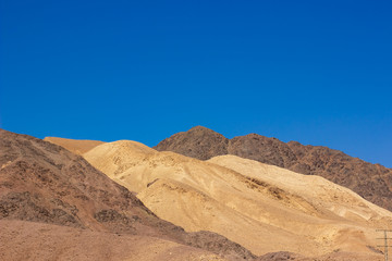 Fototapeta na wymiar Israel desert yellow and brown sand stone rocky hills simple scenery landscape photography with empty blue sky background 