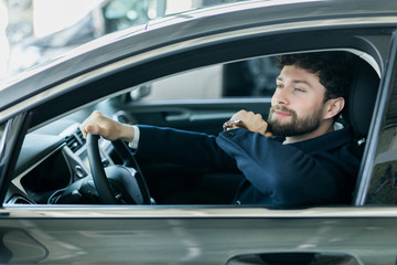 Handsome bearded man is sitting in a new car in car dealership
