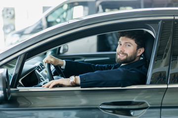 Fototapeta na wymiar Handsome bearded man is sitting in a new car in car dealership