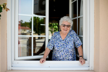 elderly senior woman opening a window of her house and welcoming people at home