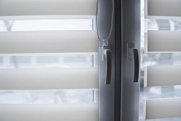 Window handle and white fabric roller blinds on the white plastic window in the living room. Close up on roll curtains indoor.