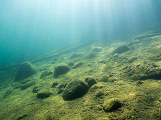 Underwater view of sloping bottom with sunrays at clear-watered lake.