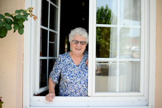 elderly senior woman opening a window of her house and welcoming people at home
